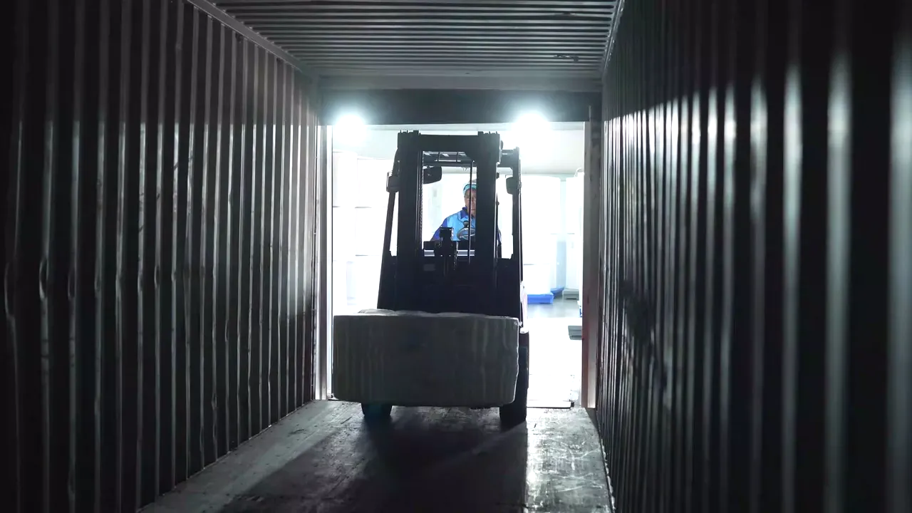 A forklift moving packaged goods into a shipping container